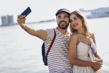 Spain, Andalusia, Malaga, happy tourist couple taking selfie with smartphone at the coast - JSMF00638