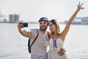 Spain, Andalusia, Malaga, happy tourist couple taking selfie with smartphone at the coast - JSMF00639