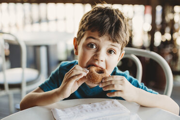 Porträt eines Jungen, der im Restaurant einen Donut isst - CAVF57802