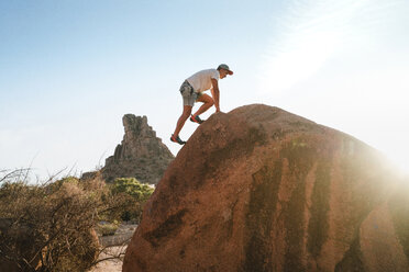 Low angle view of man climbing on rock against clear sky at desert - CAVF57810