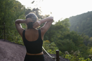 Rear view of woman tying hair while standing against mountains - CAVF57828