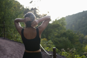 Rückansicht einer Frau, die sich die Haare bindet, während sie vor einem Berg steht - CAVF57828