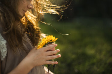 Midsection of girl holding flowers at backyard - CAVF57895