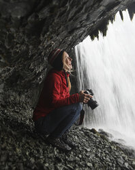Fröhliche Wanderin, die einen Wasserfall betrachtet und eine Kamera hält - CAVF57927