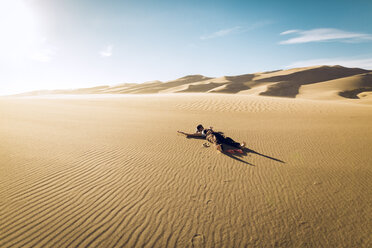 Unbeschwerte Frau im Great Sand Dunes National Park an einem sonnigen Tag im Sand liegend - CAVF57936