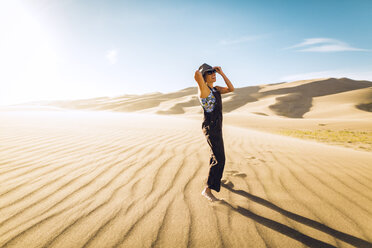 Seitenansicht einer Frau, die ihren Hut zurechtrückt, während sie an einem sonnigen Tag im Great Sand Dunes National Park steht - CAVF57937