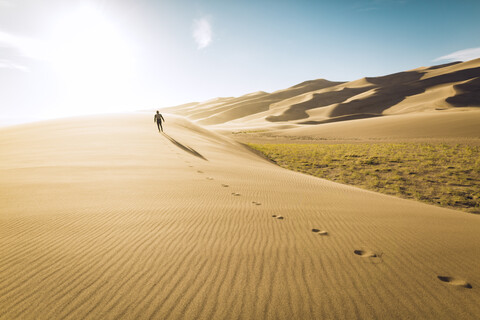 Rückansicht eines unbekümmerten Mannes, der an einem sonnigen Tag im Great Sand Dunes National Park über den Sand läuft, lizenzfreies Stockfoto