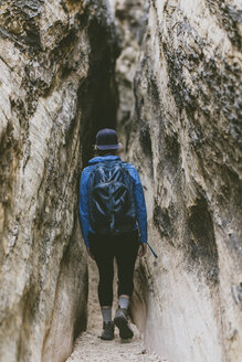 Rear view of female hiker with backpack walking amidst narrow rock formations - CAVF57952