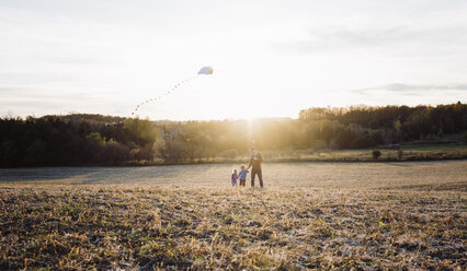 Father flying kite with children on field against sky - CAVF57961