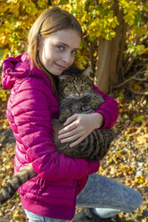 Porträt eines lächelnden Mädchens, das eine getigerte Katze im Freien im Herbst hält - SARF03996