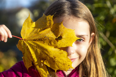 Porträt eines lächelnden Mädchens, das durch ein Loch im Herbstblatt schaut - SARF03999