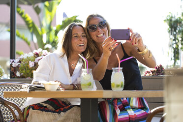 Happy girlfriends sitting outdoors with cocktail glasses taking a selfie - ERRF00234