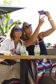 Glückliche Freundinnen sitzen mit Cocktailgläsern im Freien und machen ein Selfie - ERRF00235