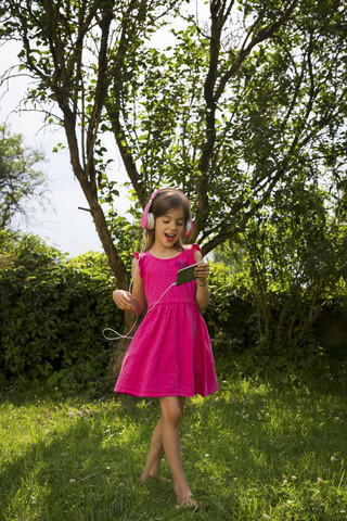 Singing girl with headphones and smartphone dancing in the garden stock photo