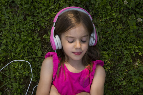 Porträt eines Mädchens, das auf einer Wiese liegt und mit rosa Kopfhörern Musik hört - LVF07576