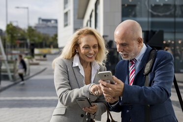 Smiling senior businessman and businesswoman using cell phones in the city - MAUF01777
