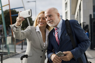 Senior businessman and businesswoman with baggage taking a selfie in the city - MAUF01778