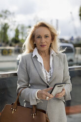 Portrait of senior businesswoman with cell phone in the city - MAUF01782