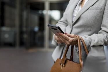 Nahaufnahme einer Geschäftsfrau mit Mobiltelefon und Handtasche - MAUF01796