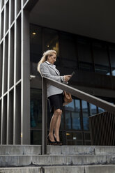 Senior businesswoman checking cell phone outside office building - MAUF01813