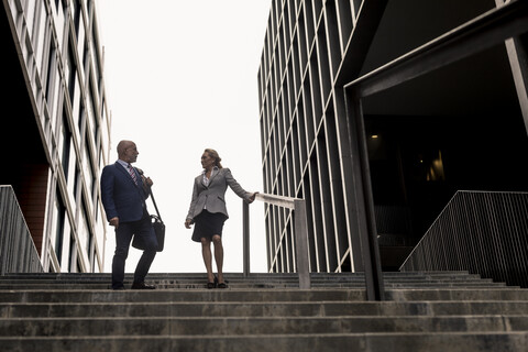 Älterer Geschäftsmann und Geschäftsfrau im Gespräch auf einer Treppe in der Stadt, lizenzfreies Stockfoto