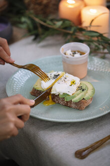 Close-up of woman cutting bread with avocado on garden table with candles - ALBF00732