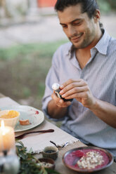 Man opening a bottle of sparkling wine at garden table - ALBF00739