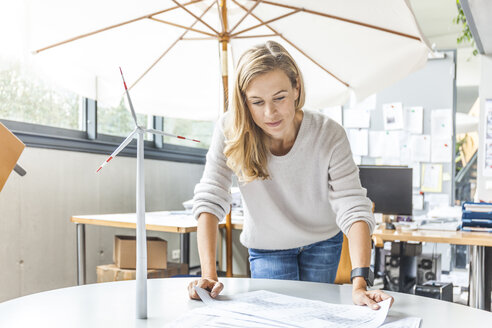 Frau im Büro arbeitet an einem Plan mit einem Windradmodell auf dem Tisch - TCF06009