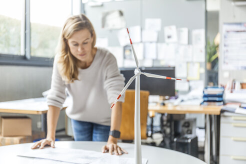 Frau im Büro arbeitet an einem Plan mit einem Windradmodell auf dem Tisch - TCF06010