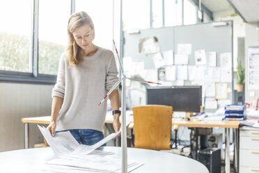 Woman in office working on plan with wind turbine model on table - TCF06011