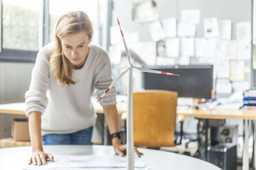 Woman in office working on plan with wind turbine model on table - TCF06012