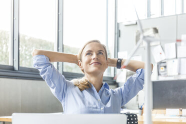 Lächelnde Frau im Büro mit Windkraftanlagenmodell im Vordergrund - TCF06016