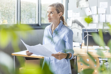 Frau im Büro arbeitet an einem Plan mit einem Windradmodell auf dem Tisch - TCF06026