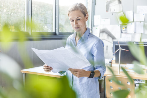 Frau im Büro arbeitet an einem Plan mit einem Windradmodell auf dem Tisch - TCF06028