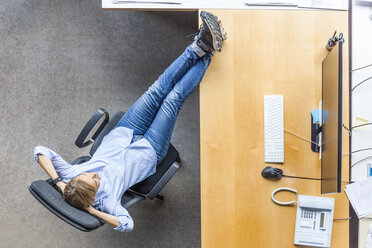 Draufsicht auf eine Frau, die sich auf einem Stuhl am Schreibtisch im Büro entspannt - TCF06036