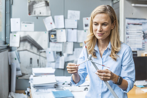 Selbstbewusste Frau im Büro, die ein Windradmodell hält, lizenzfreies Stockfoto