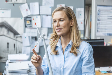 Confident woman in office holding wind turbine model - TCF06042