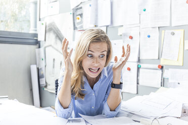 Angry woman sitting at desk in office surrounded by paperwork - TCF06047