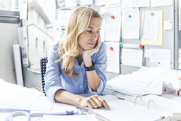 Pensive woman sitting at desk in office surrounded by paperwork - TCF06049