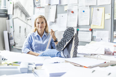 Frau entspannt sich am Schreibtisch im Büro, umgeben von Papierkram - TCF06052