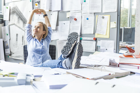 Woman relaxing at desk in office surrounded by paperwork - TCF06053