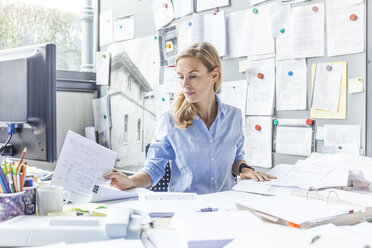 Woman sitting at desk in office doing paperwork - TCF06054