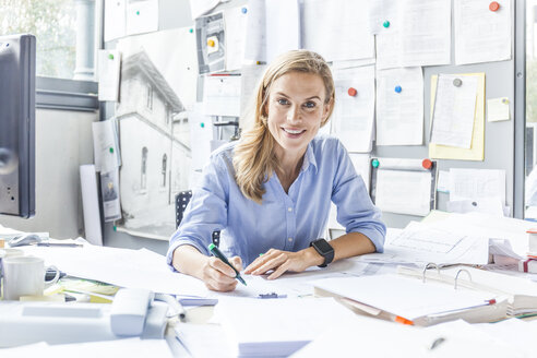 Porträt einer lächelnden Frau, die Papierkram am Schreibtisch im Büro erledigt - TCF06055