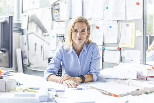 Portrait of confident woman sitting at desk in office surrounded by paperwork - TCF06056