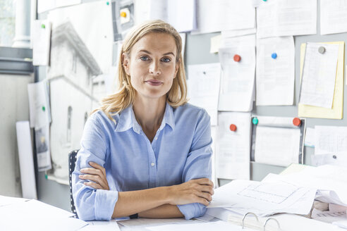Portrait of confident woman sitting at desk in office surrounded by paperwork - TCF06058