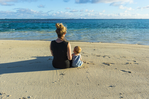 Cook-Inseln, Rarotonga, Frau sitzt mit ihrem Baby an einem weißen Sandstrand, lizenzfreies Stockfoto