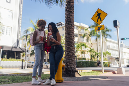 USA, Florida, Miami Beach, zwei glückliche Freundinnen mit Handy und Softdrink in der Stadt - BOYF01174