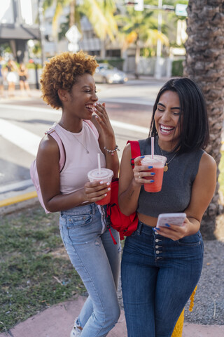 USA, Florida, Miami Beach, two happy female friends with cell phone and soft drink in the city stock photo