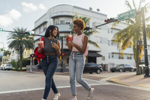USA, Florida, Miami Beach, zwei glückliche Freundinnen, die mit einem Softdrink die Straße überqueren - BOYF01177