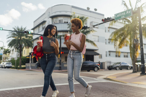 USA, Florida, Miami Beach, two happy female friends having a soft drink crossing the street - BOYF01177